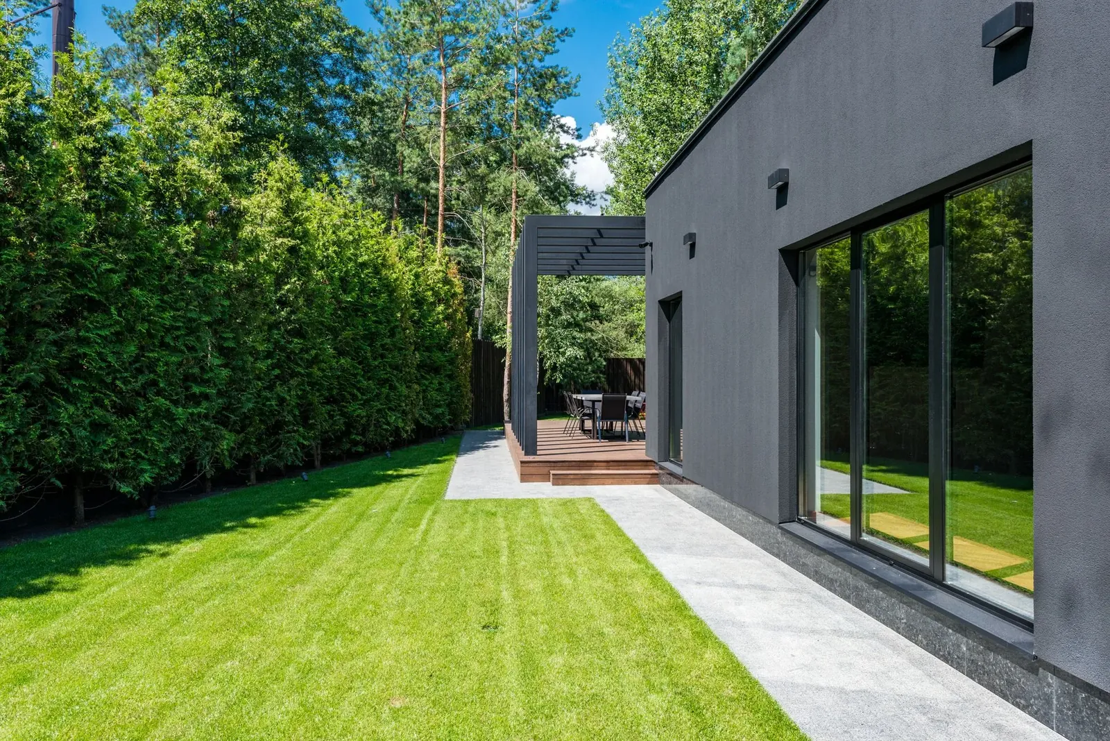 A modern house with a freshly mown striped lawn, clipped hedge and a clean paved outdoor seating area